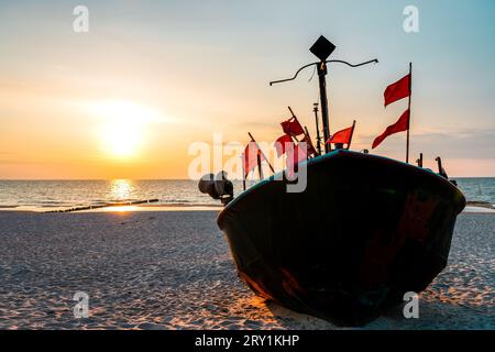 Sonnenuntergang am Strand an der polnischen Ostsee. Fischerboot am Abend in der Nähe von Międzyzdroje, Polen. Stockfoto