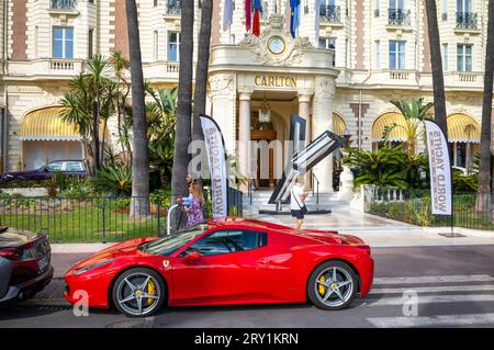 Ein roter Ferrari-Sportwagen parkt vor dem luxuriösen Carlton Hotel am Boulevard de la Croisette, direkt gegenüber dem Mittelmeer Stockfoto