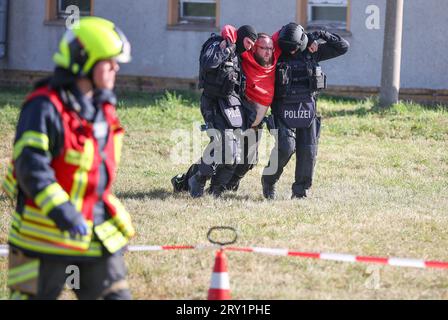 28. September 2023, Sachsen, Wiederau: Offiziere der Einheit Lebel (lebensbedrohliche Einsatzsituationen) retten einen Mann, der einen Verletzten vertritt, während einer Terrorübung aus einer Kaserne. Rund 150 Auszubildende des Deutschen Roten Kreuzes, Samariter und Johanniter aus Sachsen und Sachsen-Anhalt nehmen am Ende einer Trainingswoche an einer inszenierten Terrorsituation Teil. Es gab einen Angriff mit zahlreichen Opfern: Der Täter hat sich verwurzelt, Schüsse werden abgefeuert, es gibt Rauch, schwer bewaffnete und verhüllte Polizisten stürmen das Gebäude. Danach müssen die Notärzte das inj behandeln Stockfoto