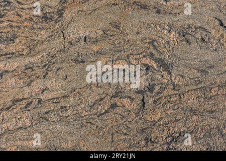 Braune Granitstruktur mit gewellten geschwungenen Linien und einem kleinen Linienbruch. Hintergrundmuster Naturstein mit braunem Verlauf. Helle und dunkle Flecken Stockfoto