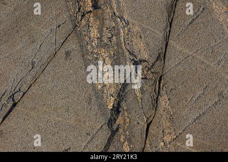 Hintergrundmuster von Granit mit Linien, die in unstrukturierten Diskontinuitäten verlaufen. Naturstein mit braunem Verlauf. Hellgelbe orangefarbene Flecken Stockfoto