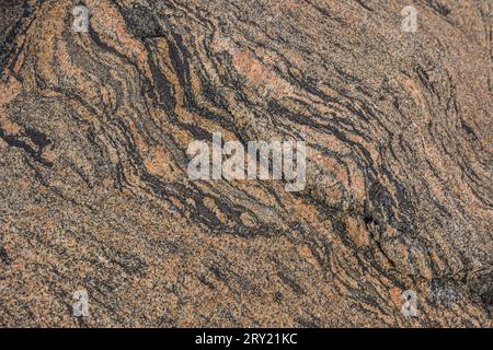 Granitoberfläche in brauner Farbe. Steinstruktur mit wellenförmigen, schräg geschwungenen Linien und einem kleinen Linienbruch. Hintergrundmuster Naturstein mit Braun Stockfoto