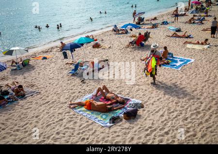 Ein Strandverkäufer geht an Menschen vorbei, die sich am öffentlichen Strand Zamenhof in Cannes an der Cote d'Azur im Süden Frankreichs entspannen. Stockfoto