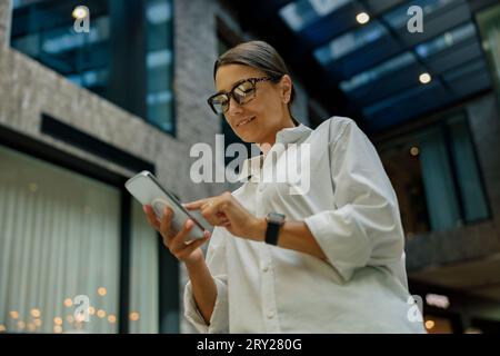 Fokussierte Unternehmerin nutzt Mobiltelefon, während sie im Büro steht Stockfoto