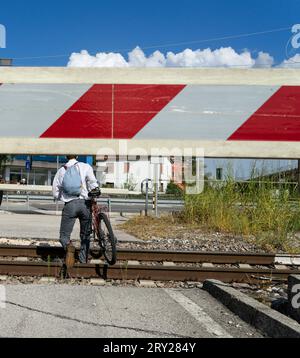 Ein Mann mit Fahrrad überquert Bahngleise, während die Querstrebe an einem ferngesteuerten Bahnübergang abgesenkt wird Stockfoto