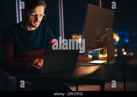 Webdesigner, der spät in einem Büro arbeitet und sein Notebook benutzt, um ein Projekt abzuschließen. Geschäftsmann sitzt an seinem Schreibtisch und nutzt die ruhige nächtliche Atmosp Stockfoto