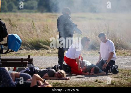 28. September 2023, Sachsen, Wiederau: Polizeibeamte sichern den Perimeter bei einer Terrorübung, während Rettungskräfte sich um die Verletzten kümmern. Rund 150 Auszubildende des Deutschen Roten Kreuzes, Samariter und Johanniter aus Sachsen und Sachsen-Anhalt nehmen am Ende einer Trainingswoche an einer inszenierten Terrorsituation Teil. Es gab einen Angriff mit zahlreichen Opfern: Der Täter hat sich verwurzelt, Schüsse werden abgefeuert, es gibt Rauch, schwer bewaffnete und verhüllte Polizisten stürmen das Gebäude. Danach müssen die Notärzte die Verletzten behandeln. Foto: Jan Woitas/dpa Stockfoto