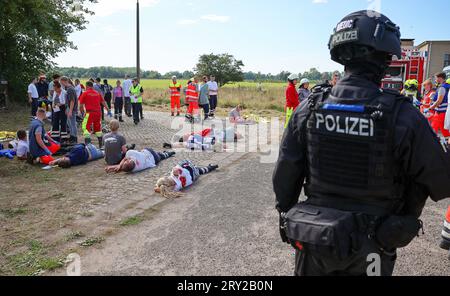 28. September 2023, Sachsen, Wiederau: Ein Polizeibeamter sichert den Perimeter während einer Terrorübung, während Rettungskräfte sich um die Verletzten kümmern. Rund 150 Auszubildende des Deutschen Roten Kreuzes, Samariter und Johanniter aus Sachsen und Sachsen-Anhalt nehmen am Ende einer Trainingswoche an einer inszenierten Terrorsituation Teil. Es gab einen Angriff mit zahlreichen Opfern: Der Täter hat sich verwurzelt, Schüsse werden abgefeuert, es gibt Rauch, schwer bewaffnete und verhüllte Polizisten stürmen das Gebäude. Danach müssen die Notärzte die Verletzten behandeln. Foto: Jan Woitas/dpa Stockfoto