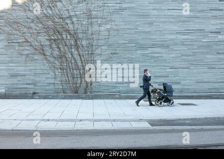 Ein Mann in einem Anzug, der am Nationalmuseum in Oslo vorbeiläuft und einen Kinderwagen schiebt. Stockfoto