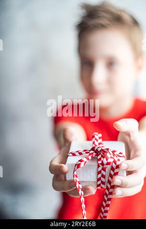 Verschwommenes Kind mit einer kleinen Geschenkbox mit rotem Band während der Weihnachtsfeier vor verschwommenem Hintergrund Stockfoto