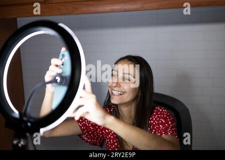 Fröhliche Frau bereitet Smartphone auf einem Stativ mit Ringlampe vor, bevor sie Vlog aufnimmt Stockfoto