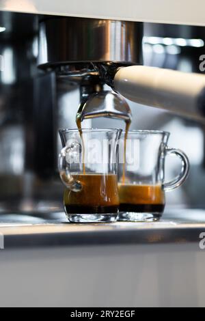 Heißer, frischer Espresso, der in zwei Glasbechern aus der Kaffeemaschine auf der Theke fließt Stockfoto