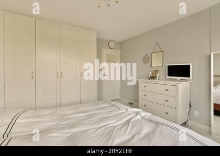 Inneneinrichtung eines modernen Schlafzimmers mit gemütlichem Bett und Kommode mit Fernseher neben großem Kleiderschrank im geräumigen Haus Stockfoto