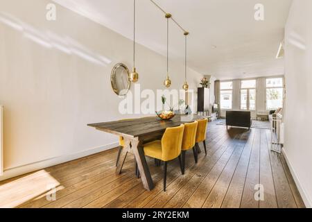 Das geräumige Apartment verfügt über ein Esszimmer mit Lichtern über einem Holztisch und gelben Stühlen, die auf Holzboden angeordnet sind Stockfoto