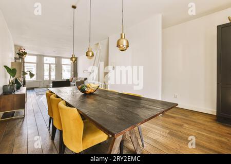 Modernes Esszimmer mit Lichtern über Holztisch und gelben Stühlen auf Parkettboden in geräumigem Apartment Stockfoto