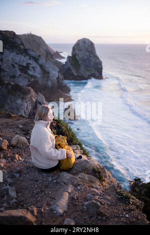 Eine Frau blickt auf den Ozean, der auf den Klippen in Portugal sitzt. Stockfoto