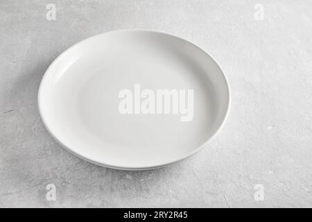 Leere weiße Keramikplatte auf grauem Betontisch, Hochwinkel. Vorlage für die Präsentation von Speisen und Restaurantmenüs. Stockfoto