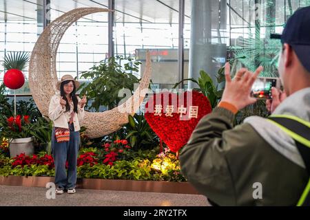 Peking, chinesische Provinz Yunnan. September 2023 27. Ein Passagier posiert für Fotos vor Blumendekorationen am Kunming Changshui International Airport in Kunming, Südwestchinas Provinz Yunnan, 27. September 2023. Das Mid-Autumn Festival und die Feiertage am Nationalfeiertag, die vom 29. September bis zum 6. Oktober dieses Jahres dauern, sind eine Spitzenreisezeit und Tourismussaison in China. Quelle: Cui Wen/Xinhua/Alamy Live News Stockfoto