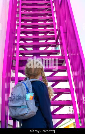 Schulmädchen steigt die Treppe. Konzept Schultage, Starttermin, nächste Stufe, Karriereleiter, der Beginn des Weges. Mädchen in einer Uniform mit Rucksack Stockfoto