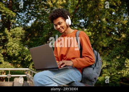 Glücklicher lächelnder Student, der kabellose Kopfhörer mit Laptop trägt Stockfoto