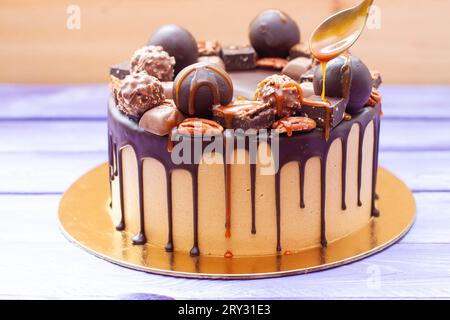 Nahaufnahme der Frau, die gesalzene Karamellsauce auf den Schokoladenkuchen gießt, dekoriert mit Süßigkeiten, Trüffeln, Keksen und Nüssen Stockfoto