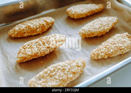 Rohe gefrorene panierte Hühnerstücke auf einem Backblech. Stockfoto