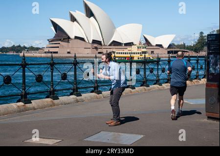 25.09.2019, Sydney, New South Wales, Australien - Ein Mann hält ein Eis in der Hand und macht ein Foto mit seinem Handy, während ein Jogger vorbeiläuft. Stockfoto