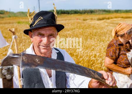 Muzlja, Vojvodina, Serbien, 02. Juli 2022; XXXIX traditionelles Mähen von Weizen. Das Porträt eines erfahrenen Landwirts, der bereit für die Ernte ist, hält die Sense vor sich Stockfoto