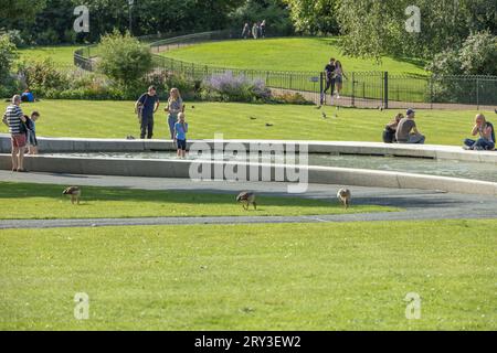 Sonniger Tag in London am Princess Diana Memorial Fountain mit Familien und Paaren, die den Brunnen genießen und durch den Hyde Park spazieren gehen. Stockfoto