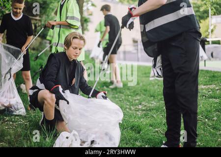 Junge kniet vor einem Freund und sammelt Müll in der Tasche Stockfoto