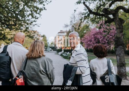 Porträt eines lächelnden älteren Mannes, der über die Schulter schaut, während er mit Freunden im Park spaziert Stockfoto