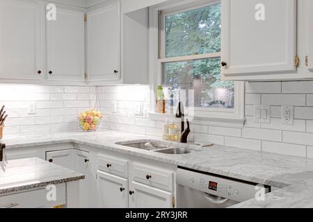 Saubere, moderne weiße Küche mit Steinarbeitsplatten und Granit Rolling Island. Obstkorb in der Ecke mit leeren Zählern Stockfoto