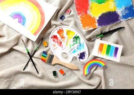 Künstlerpalette und Pinsel mit Farben und Zeichnungen auf Textilhintergrund Stockfoto
