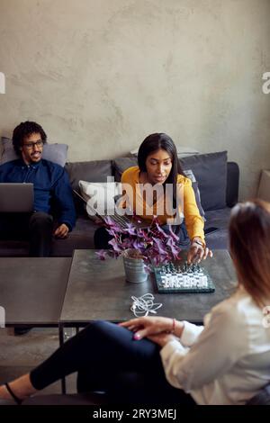 Weibliche Profis spielen Schach in der Nähe eines Geschäftsmannes im Kreativbüro Stockfoto