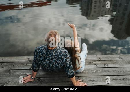 Rückansicht eines Mädchens, das zeigt, während er mit Großvater auf dem Steg sitzt Stockfoto