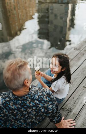 Hochwinkelansicht eines Mädchens mit Eiskegel, während er Großvater auf dem Steg betrachtet Stockfoto