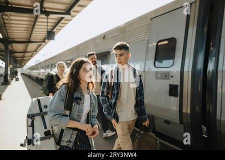 Junge, der mit einem Mädchen spricht, das Gepäck trägt, während er in den Urlaub geht Stockfoto