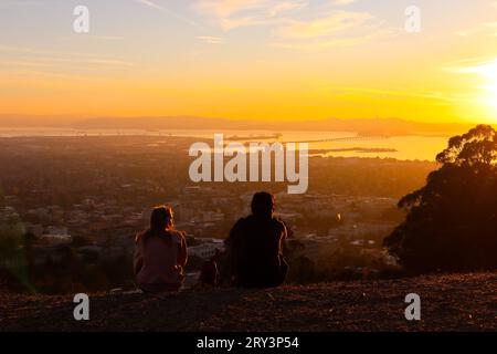 Die Menschen genießen es, den Sonnenuntergang am goldenen Himmel zu sehen. Das Bild wurde auf dem Grizzly Peak (Berkeley Hill) mit Pazifik und Bay Bridge im fernen Hintergrund aufgenommen. Stockfoto