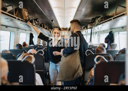Lächelnde Frau, die mit dem Mann spricht, während sie zwischen den Sitzen im Zug steht Stockfoto