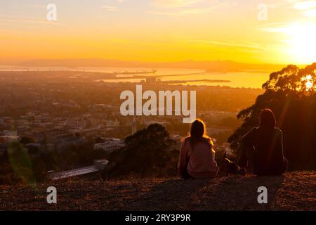 Die Menschen genießen es, den Sonnenuntergang am goldenen Himmel zu sehen. Das Bild wurde auf dem Grizzly Peak (Berkeley Hill) mit Pazifik und Bay Bridge im fernen Hintergrund aufgenommen. Stockfoto