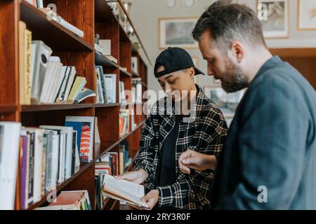 Junger Mann, der mit Professor in der Bibliothek über Buch diskutiert Stockfoto