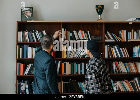 Reifer männlicher Professor, der nach einem Buch greift, während er in der Bibliothek steht Stockfoto