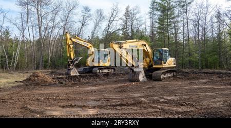 CROW WING CO, MN - 10. MAI 2023: Freiliegender brauner Boden auf einem leeren, zukünftigen Neubaugrundstück und zwei gelbe Komatsu-Bagger in Seitenansicht. Stockfoto