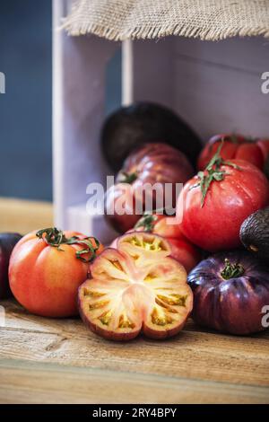 Stillleben von Tomaten verschiedener Art mit etwas geschnittenem, rosafarbenem Holzkasten auf einem Holzbrett Stockfoto