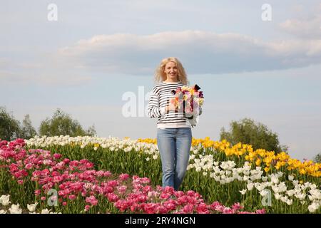 Glückliche Frau mit Frühlingsstrauß von Blumen in schönem Tulpenfeld an sonnigen Tagen Stockfoto