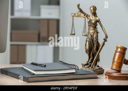 Figur der Lady Justice, Hammer und Notizbücher auf Holztisch im Innenbereich, Platz für Text. Symbol der gerechten Behandlung nach dem Gesetz Stockfoto