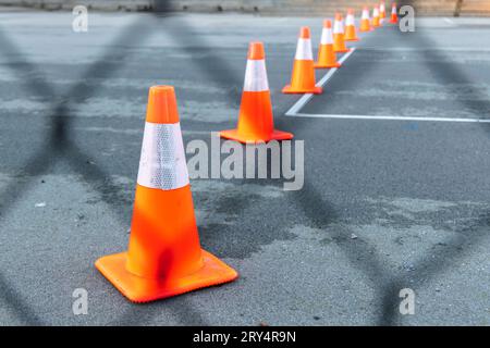 Orangefarbene und weiße Verkehrskegel in einer Reihe, die in die Entfernung gegen schwarzen Asphalt verfallen; im Vordergrund befindet sich ein Drahtzaun, der nicht fokussiert ist. Gedreht in Vancouver, Kanada Stockfoto