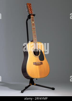 Joodee akustische 12-saitige Gitarre auf einem Ständer, angewinkelt, auf grauem Hintergrund mit Schatten Stockfoto