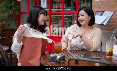 Eine fröhliche junge asiatische Plus-Size-Frau spricht gerne mit ihrem Freund, während sie sich während ihres Einkaufstages in t an einem Tisch im Freien in einem Café entspannt Stockfoto