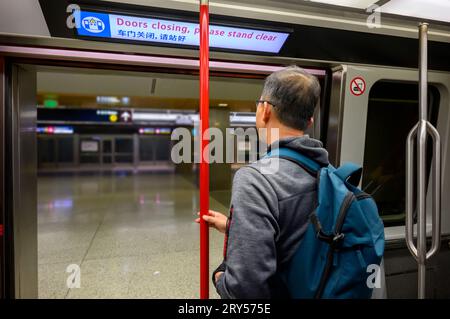 Mann, der an der offenen Tür der Flughafenbahnverbindung steht. Das Neon-Board oben mit Nachrichten in Englisch und Chinesisch - Türen schließen, bitte stehen Sie hier Stockfoto